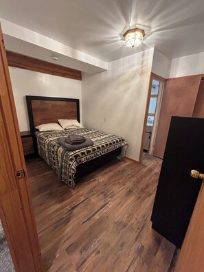 Ein Schlafzimmer mit Bett, Holzboden, einer Deckenleuchte und einer Tür.