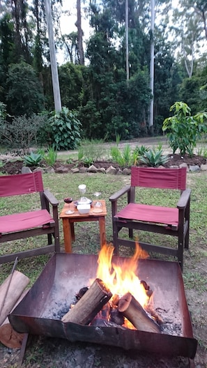 A fire pit with two wooden chairs and a small table with items on it.