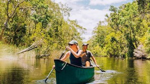 Deux personnes se trouvent dans un bateau vert sur une rivière, entourée d’arbres.