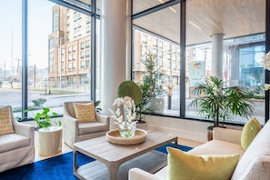 Un hall d’hôtel moderne, doté de grandes fenêtres, de sièges confortables et de plantes d’intérieur.