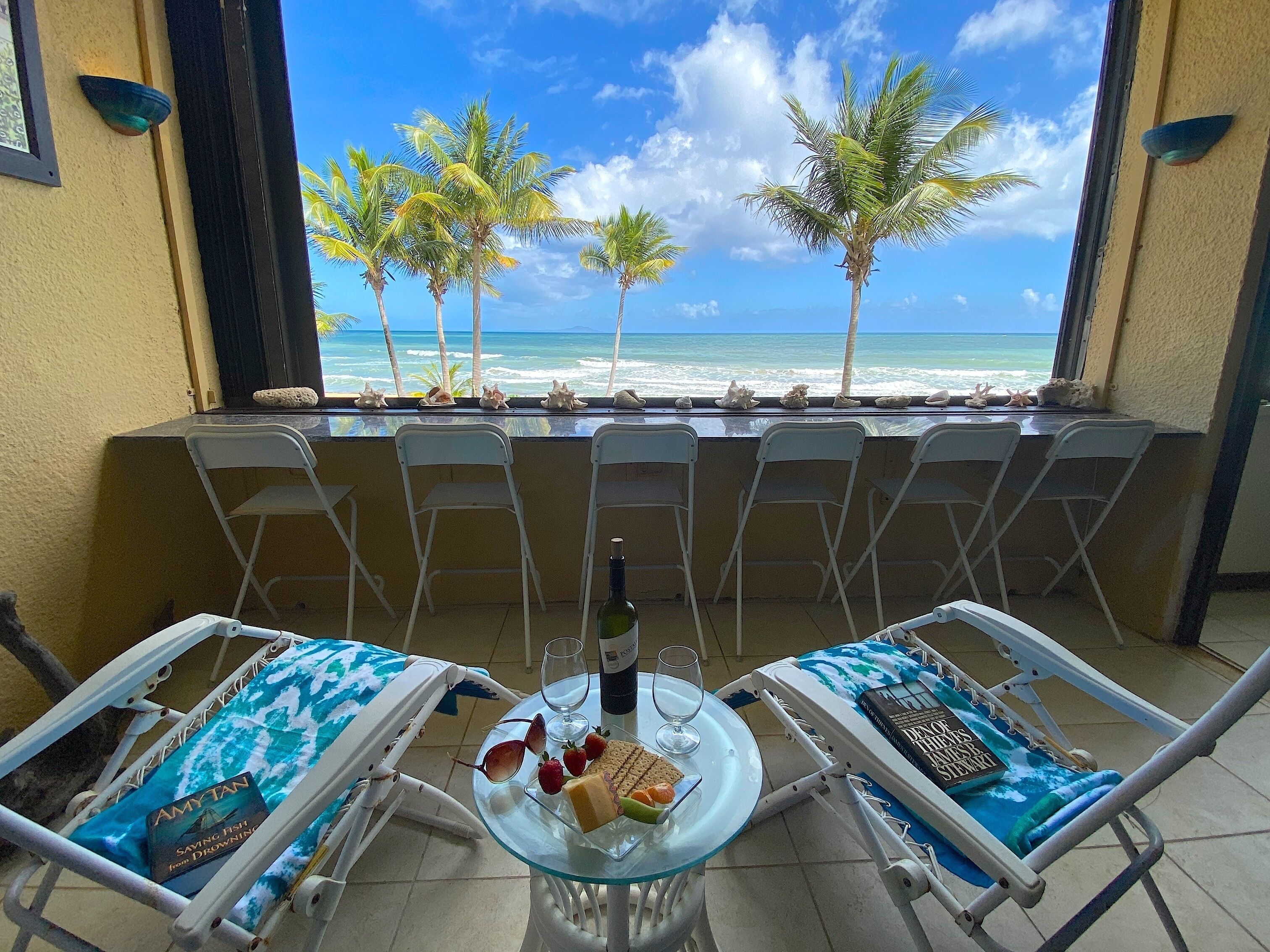A balcony with two sun loungers, a glass table with a bottle, wine glasses, and snacks.