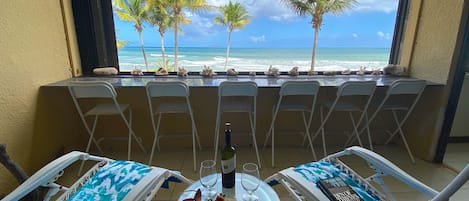 A balcony with two sun loungers, a glass table with a bottle, wine glasses, and snacks.