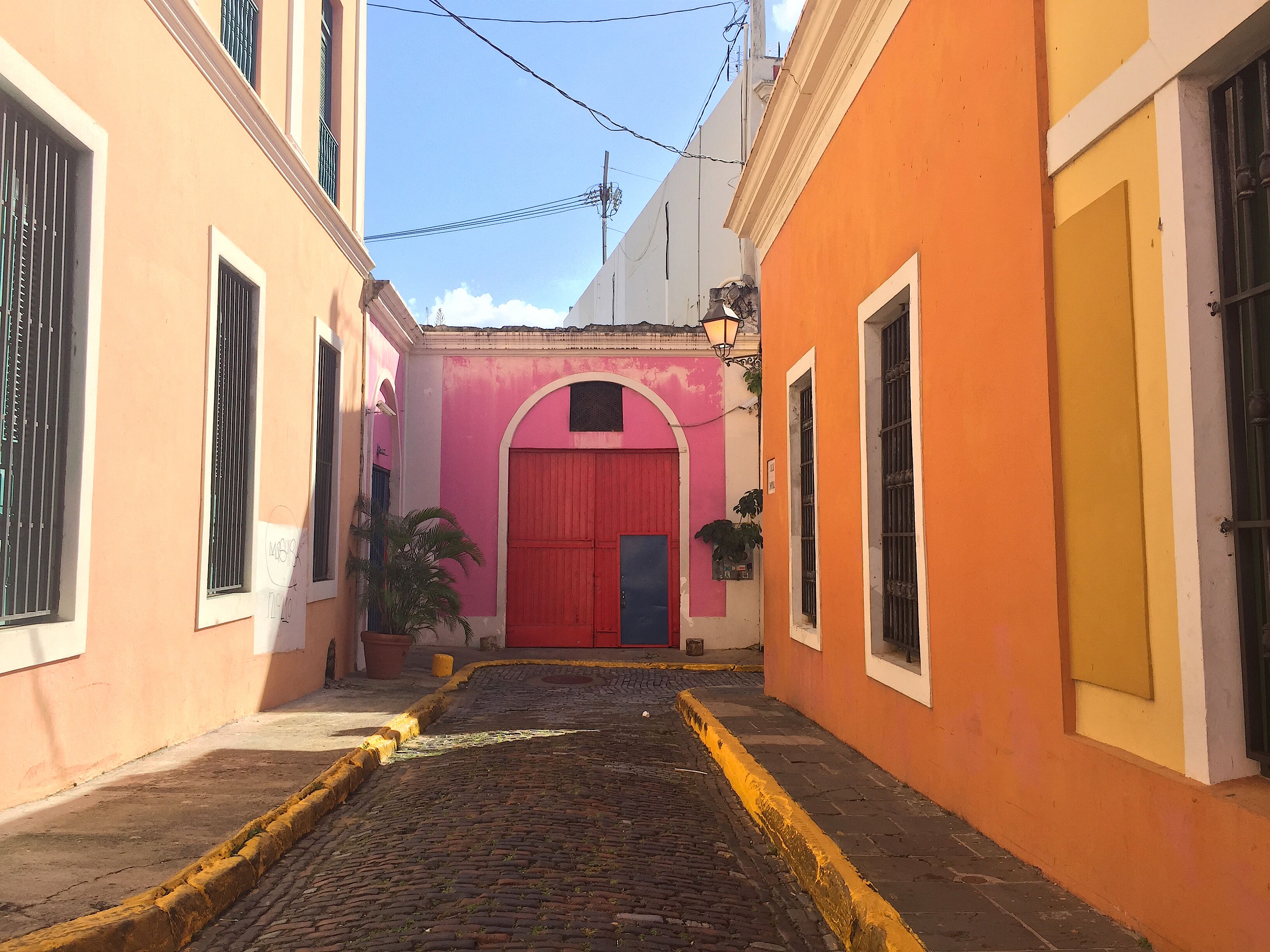 Una estrecha calle adoquinada flanqueada por edificios con fachadas de colores pastel y una puerta roja destacada.