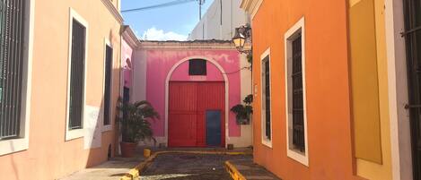 Una estrecha calle adoquinada flanqueada por edificios con fachadas de colores pastel y una puerta roja destacada.