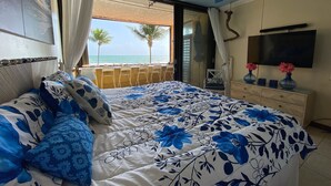 Quarto com cama, ventilador de teto, televisão e vista para o oceano.