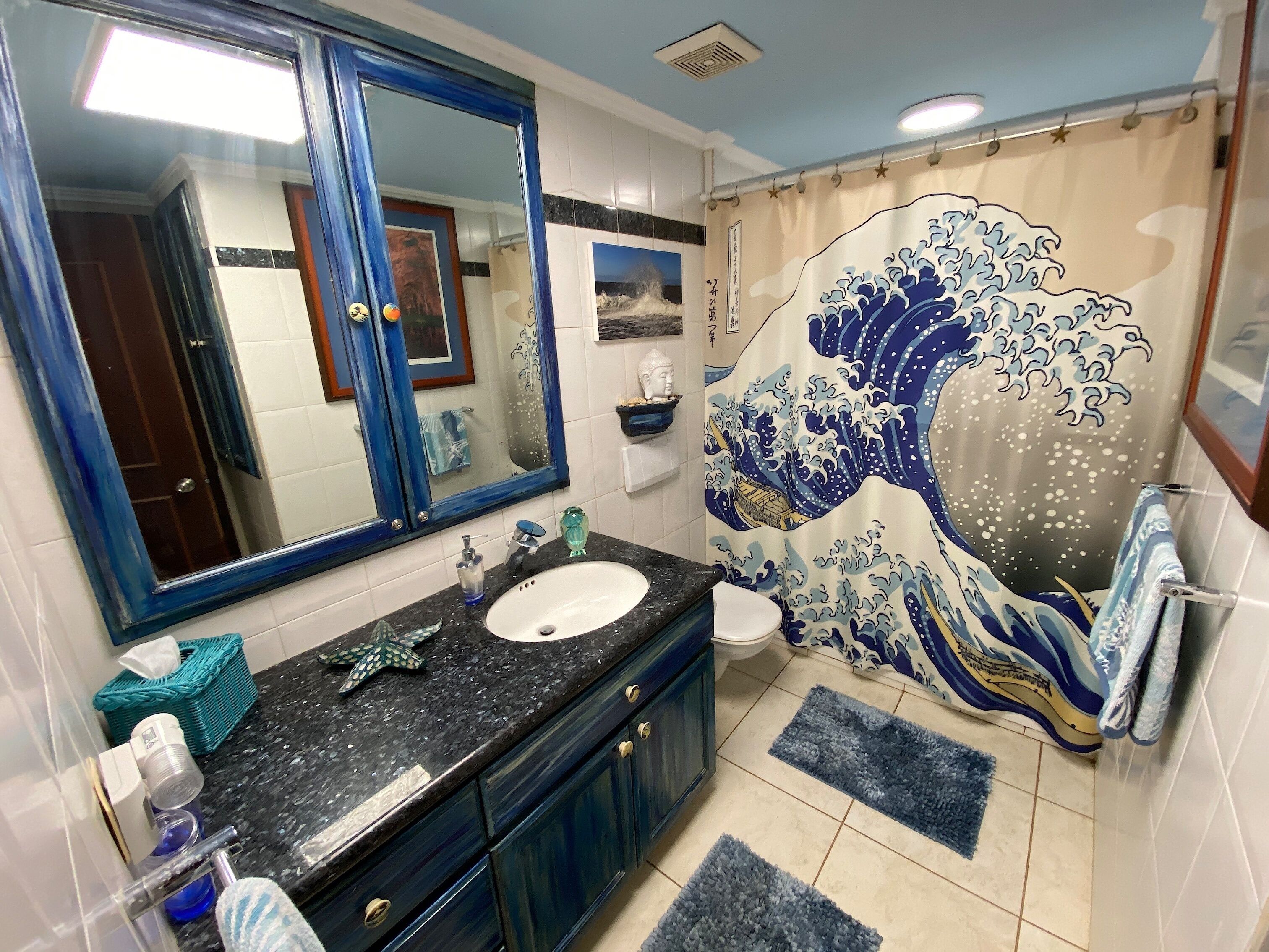 Een badkamer met een grote spiegel, een wastafel, toilet en een douchegordijn met een golfmotief.