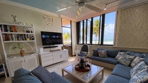 Uma sala de estar com uma televisão grande, um sofá, uma mesa de centro e uma estante de livros.