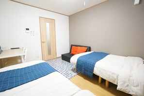 Two single beds, a desk, and a sofa are featured in this hotel room with a checkered floor.