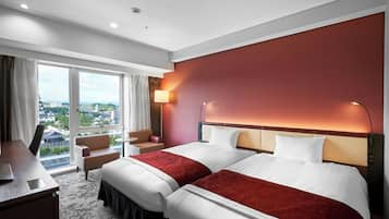A hotel room with two beds, a desk, a chair, and a view of the city.