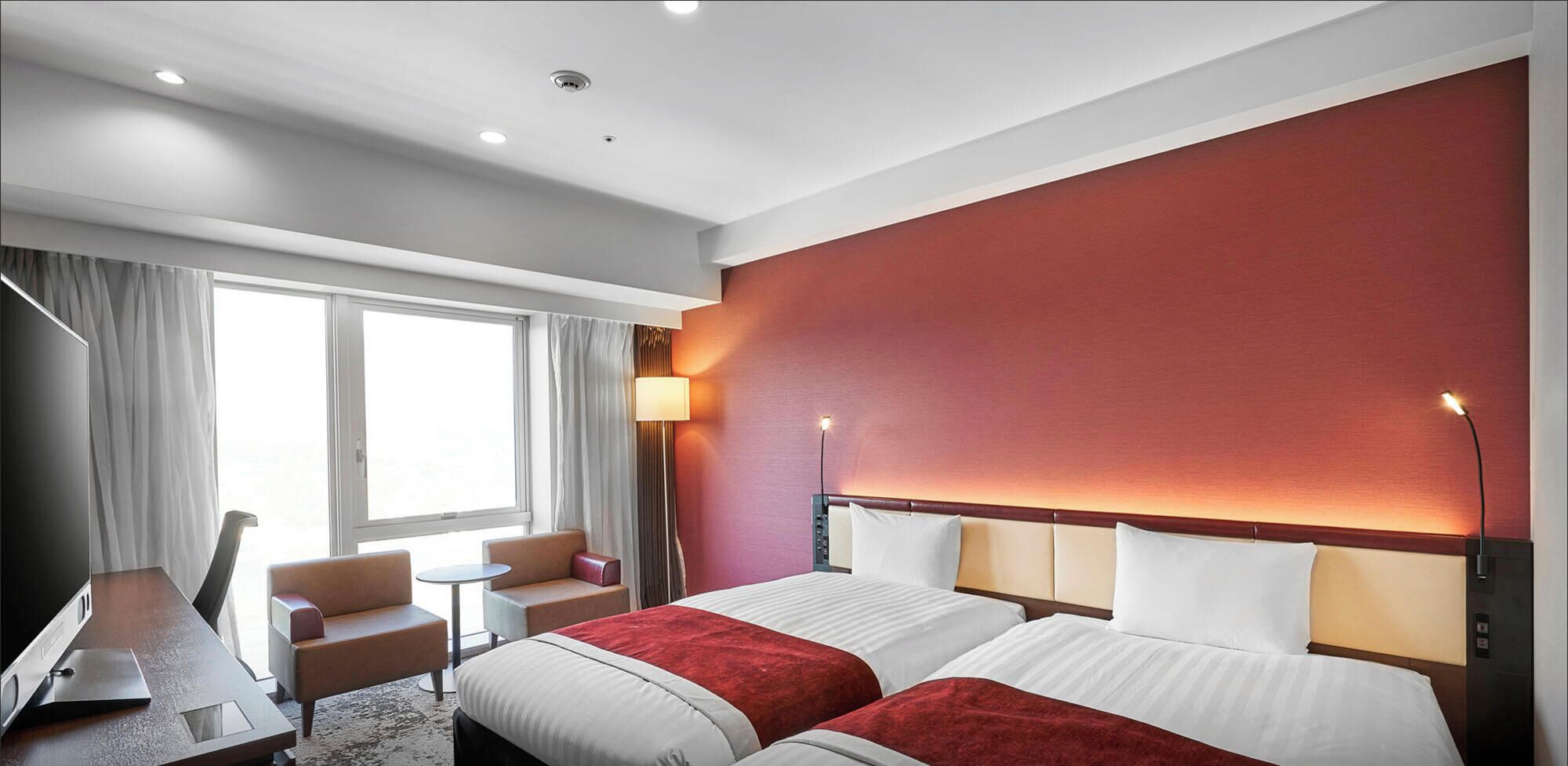 A hotel room with two beds, a desk, a chair, a small table, and a window with curtains.