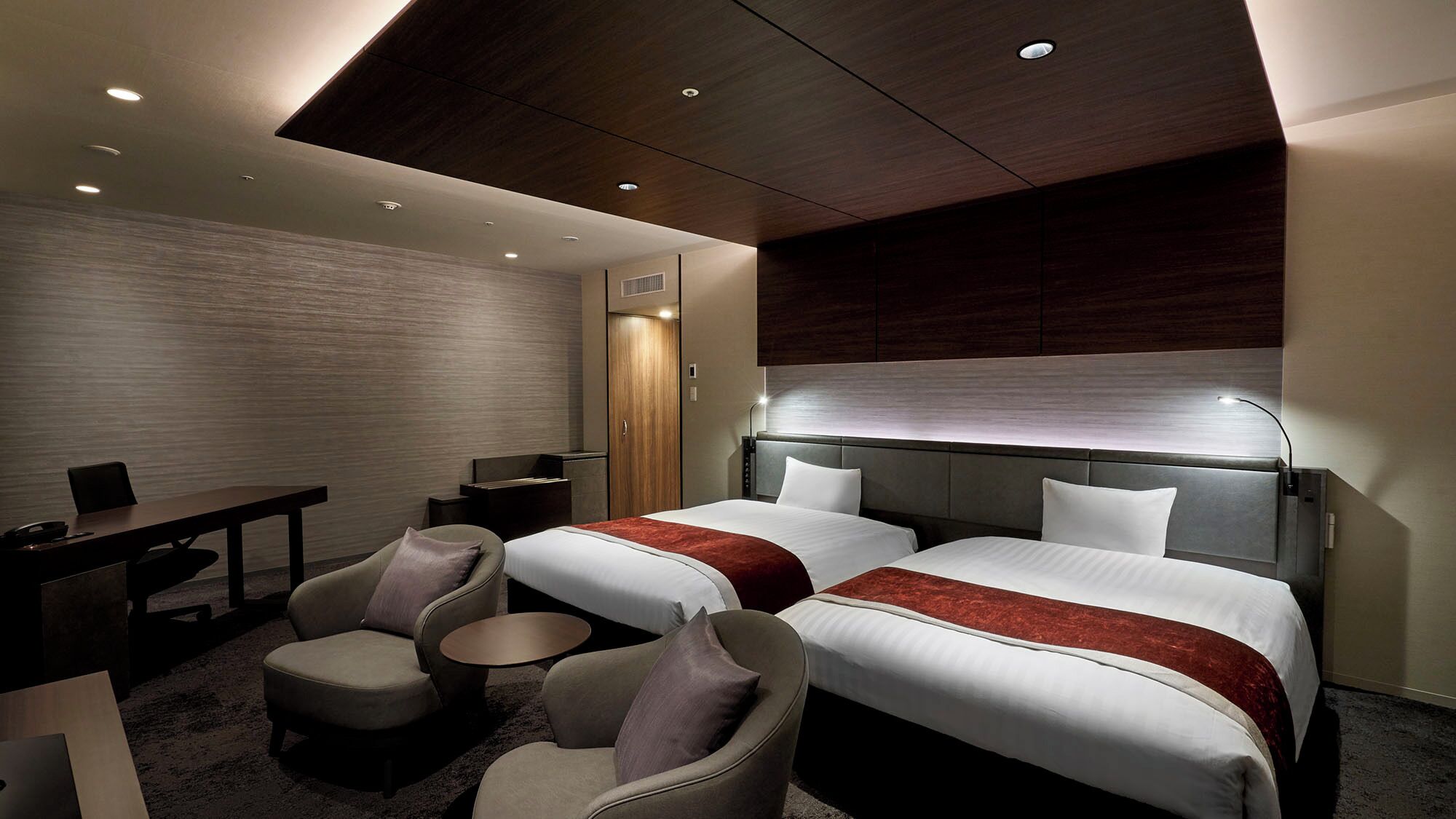 A hotel room with two beds, a desk, a chair, a round table, and a wardrobe.