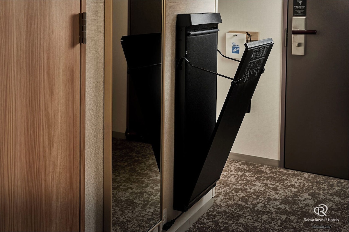 Habitación de hotel con una puerta de madera, un armario negro y un escritorio pequeño con un ordenador.
