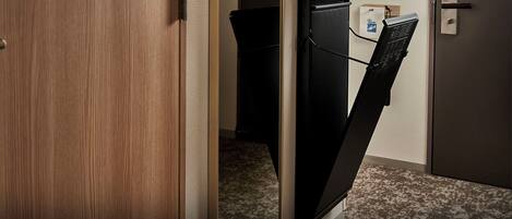 Habitación de hotel con una puerta de madera, un armario negro y un escritorio pequeño con un ordenador.