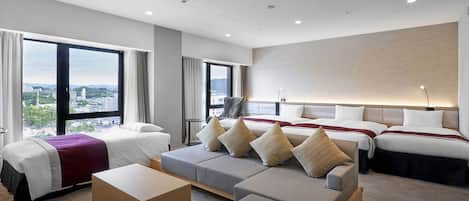 A hotel room with two beds, a sofa, a coffee table, and a view of the city.