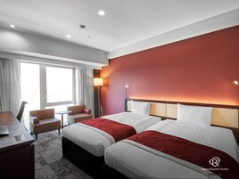 A hotel room with two beds, a desk, a chair, and a window with curtains.
