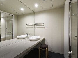 Un baño moderno con dos lavamanos, cabina de ducha con vidrio y un taburete de madera.