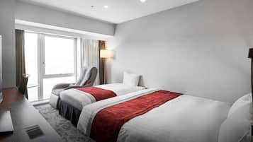 A hotel room with two beds, a desk, a chair, a lamp, and a window with curtains.