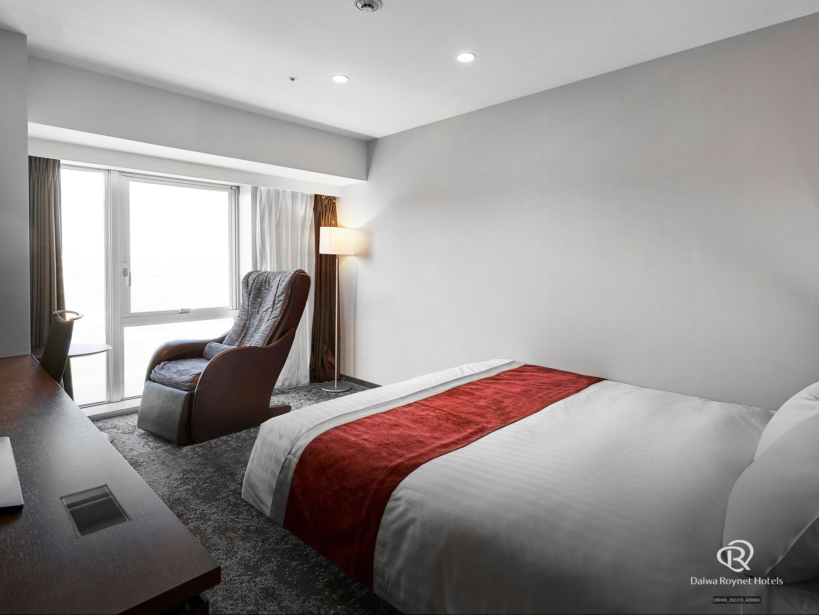A hotel room with a bed, a desk, a chair, and a window with curtains.