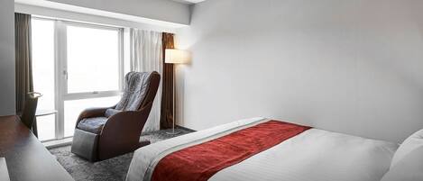 Una habitación de hotel con cama, escritorio, silla y ventana con cortinas.