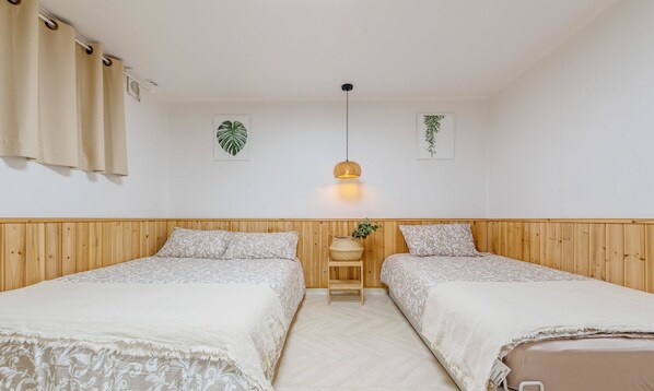 A room with two beds, wooden headboard, a small table with a plant, and a hanging light fixture. - SeeU House (Seoul)