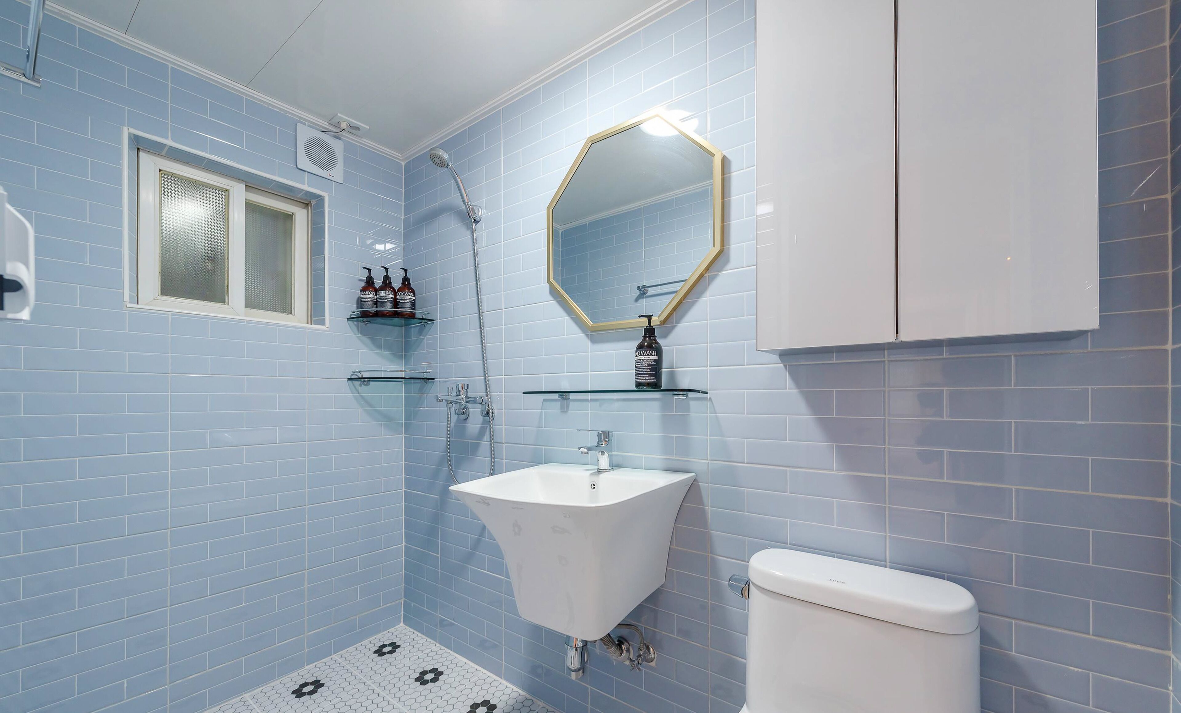 Een badkamer met blauwe tegels, een wit wastafelmeubel, een toilet, een douche en een spiegel met gouden lijst.