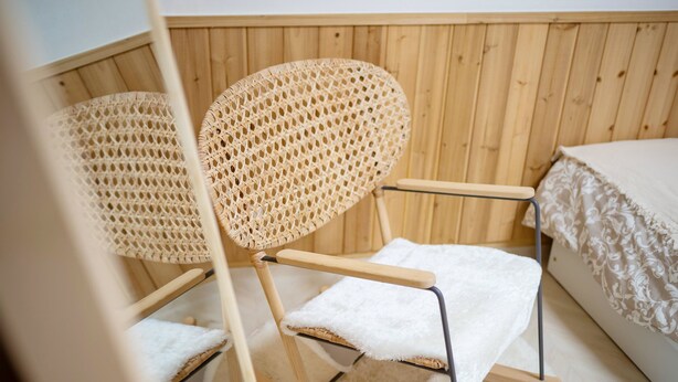 A wooden room with two wicker chairs, a bed with a white bedspread, and a wooden wall. - SeeU House (Seoul)