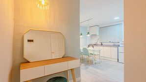 A modern kitchen with white cabinets, a dining area with a white table and chairs, and a hallway with a white door and a bench. - SeeU House (Seoul)