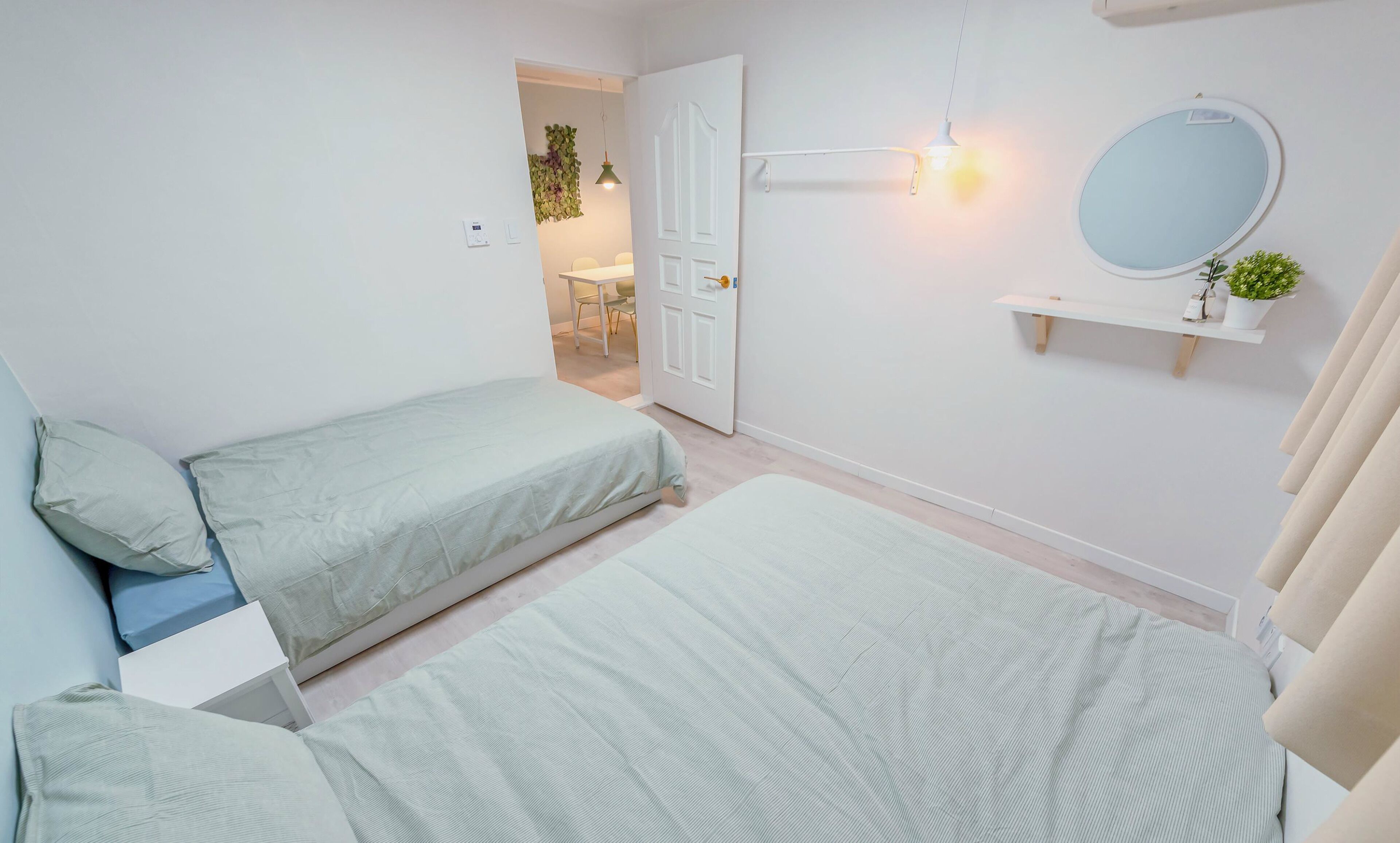 A bedroom with two single beds, a small desk, a chair, a mirror, and a shelf with a plant.