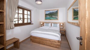 Ein Schlafzimmer mit einem hölzernen Bett, einem Fenster mit Vorhängen, einem kleinen Nachttisch und einem Bild an der Wand.