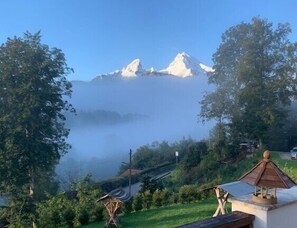 Un paysage de montagne avec des sommets enneigés, un ciel dégagé et une vue sur une maison au toit traditionnel.