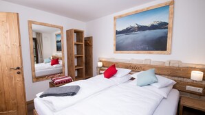Une chambre d’hôtel avec deux lits, une tête de lit en bois, un grand miroir, un tableau représentant des montagnes et une table de chevet avec une lampe.