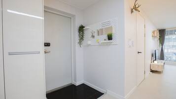 A hallway with a white door, a black mat at the entrance, a wall-mounted mirror, and a mounted deer head decoration.