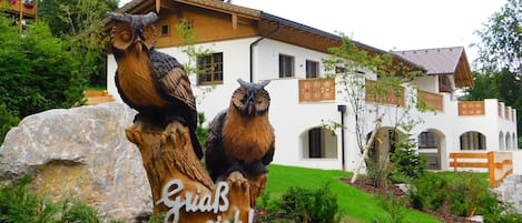 Un edificio de fachada blanca, balcones de madera y una gran roca con esculturas de búhos.