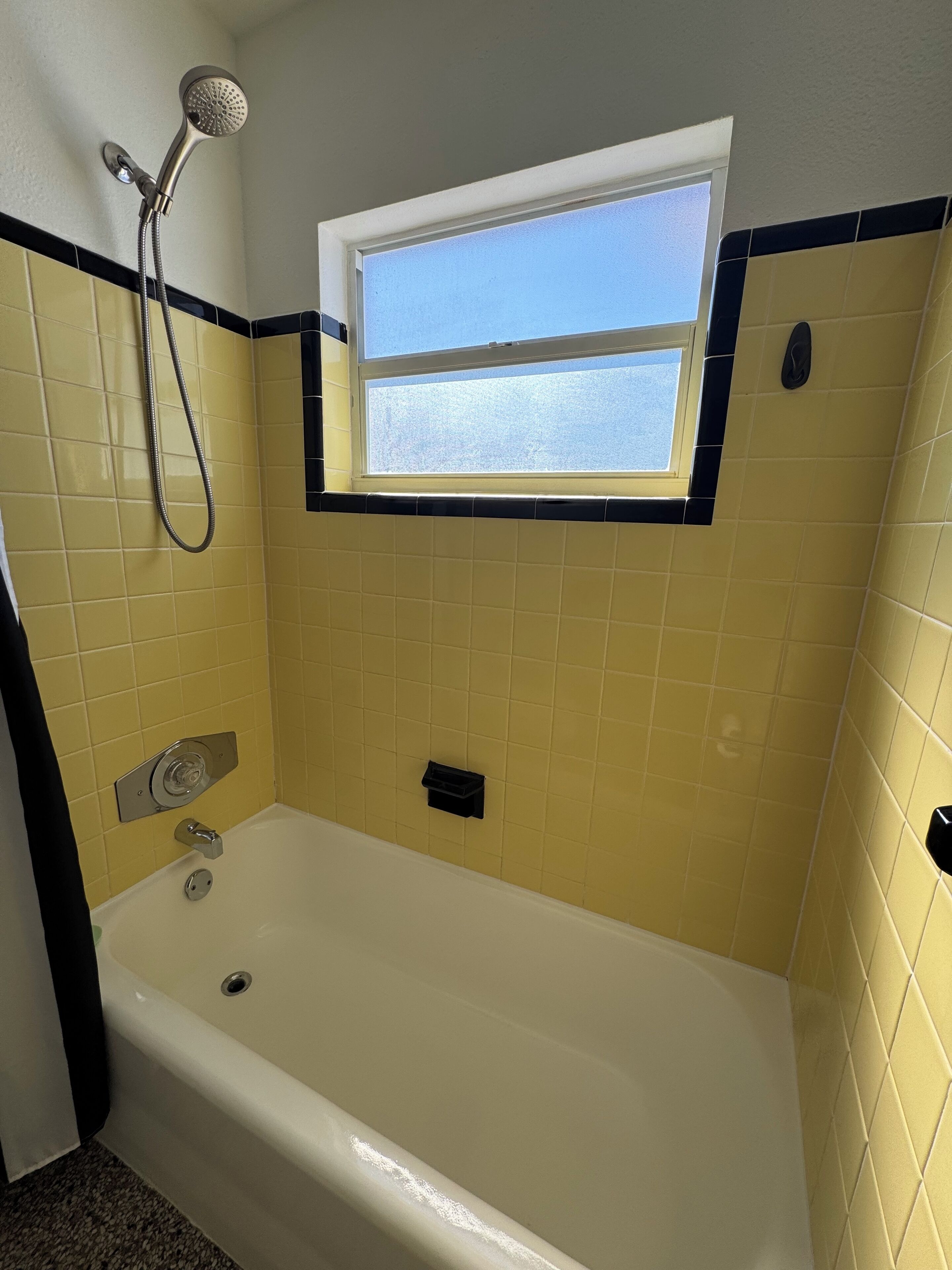 Un baño con bañera, ducha, ventana y paredes de azulejos amarillos.