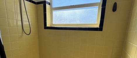 Un baño con bañera, ducha, ventana y paredes de azulejos amarillos.