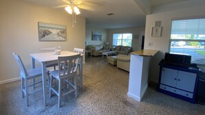 A spacious living area with a dining table, chairs, a sofa, and a coffee table. There is a ceiling fan, a microwave, and a cabinet.
