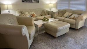 A living room with beige leather sofas, a coffee table, and a painting of a beach pathway.