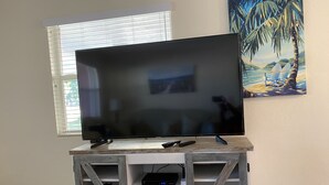 A flat-screen TV on a wooden TV stand with a seashell and remote controls.