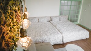 Ein Zimmer mit einem Bett, einem Nachttisch, einer Pendelleuchte und einem Fenster mit grünem Rahmen.