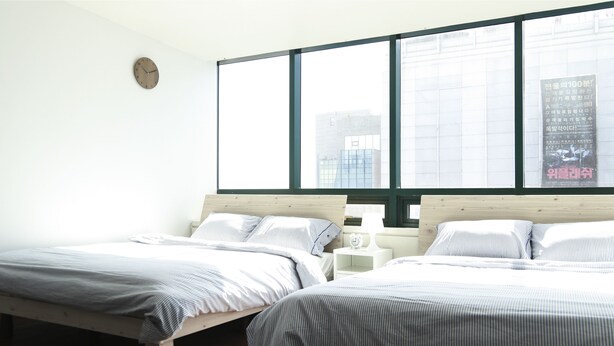 A bedroom with two beds, a large window, and a wall clock. - Sweet House (Seoul)