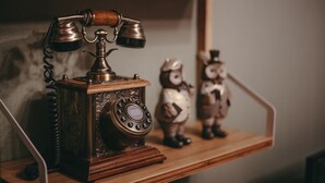 En vintagerotartelefon på en træhylde med to figurer.