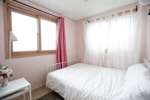 A bedroom with a single bed, a nightstand, a lamp, and a window with curtains. - Lovely House (Seoul)