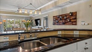 A modern kitchen with a double sink, granite countertop, and a decorative wooden wall panel. - Condo with Open Access to the Scenery from Ground Porch (Kissimmee)