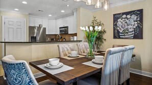 A dining area with a wooden table, white chairs, and a vase of flowers. - Condo with Open Access to the Scenery from Ground Porch (Kissimmee)