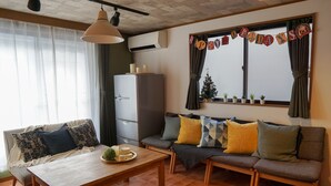 A cozy living room with a sofa, a coffee table, and a dining table. There is a window with a Christmas tree and a banner on it. - Ikken Rakutei (Tokyo)