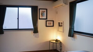 A hotel room with a bed, a small table with a lamp, and two windows with curtains. - Ikken Rakutei (Tokyo)