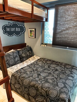 Un lit mezzanine avec une couvre-lit et des coussins à motifs, un petit tableau encadré accroché au mur et une fenêtre donnant sur les arbres.