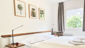 Un dormitorio ordenado con cama, mesita de noche y ventana con cortinas.