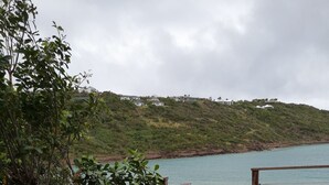 Une terrasse extérieure avec une table ronde et quatre chaises, offrant une vue sur un plan d’eau et une colline.