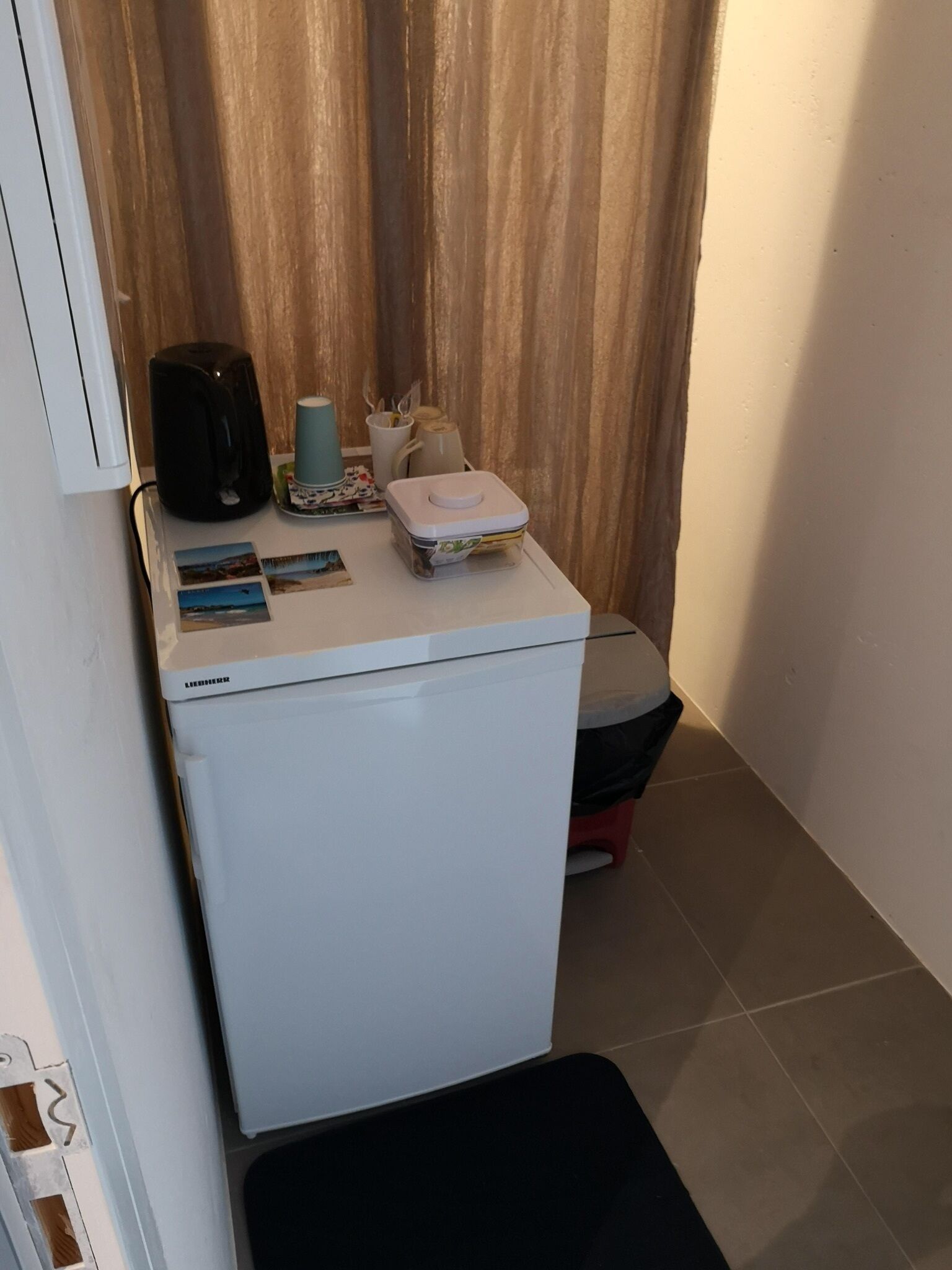 Een kleine keuken met een witte koelkast, een koffiezetapparaat, een klein spoelgedeelte en een aanrecht met enkele spullen.